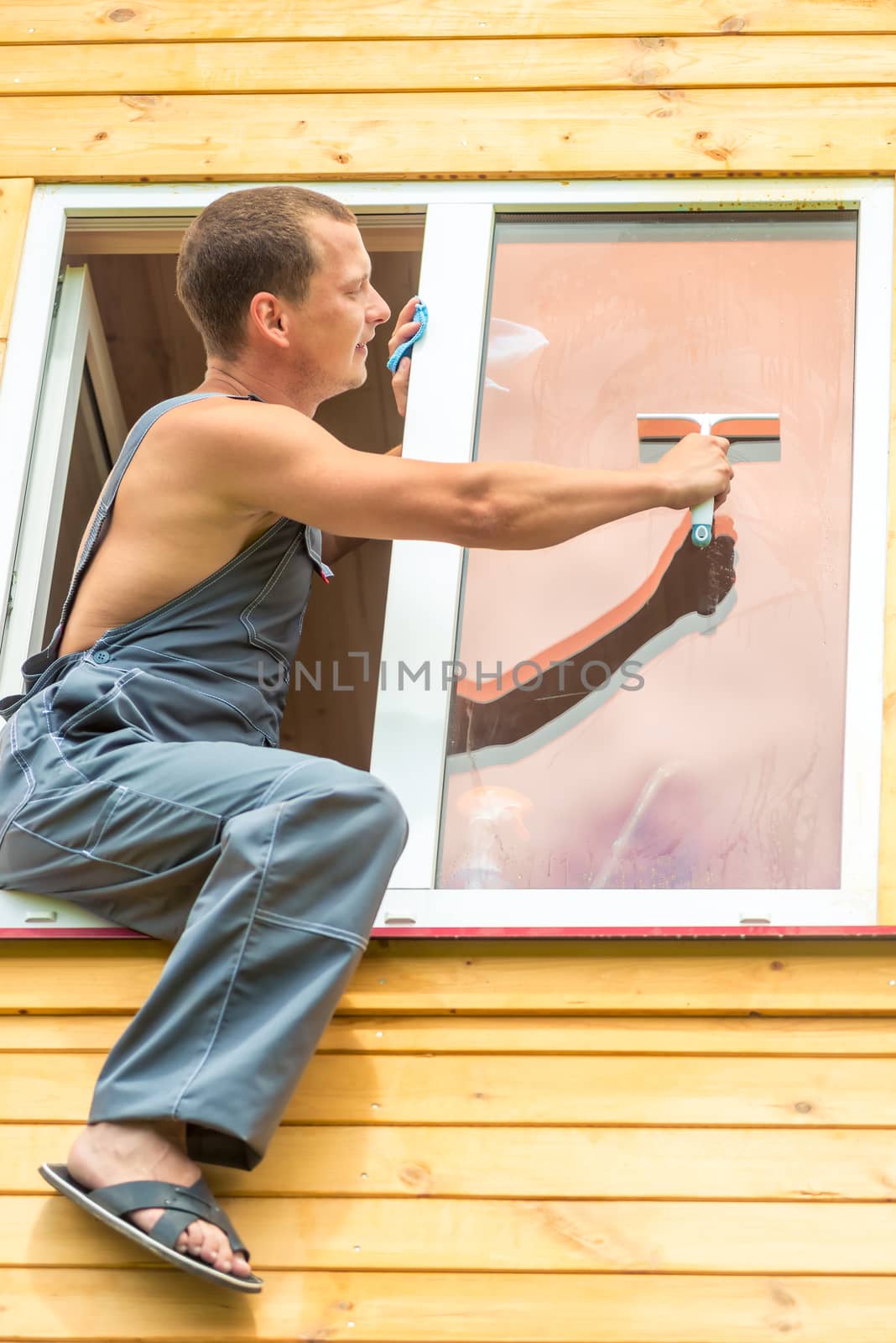 Male professional in overalls cleans the window in the house by kosmsos111