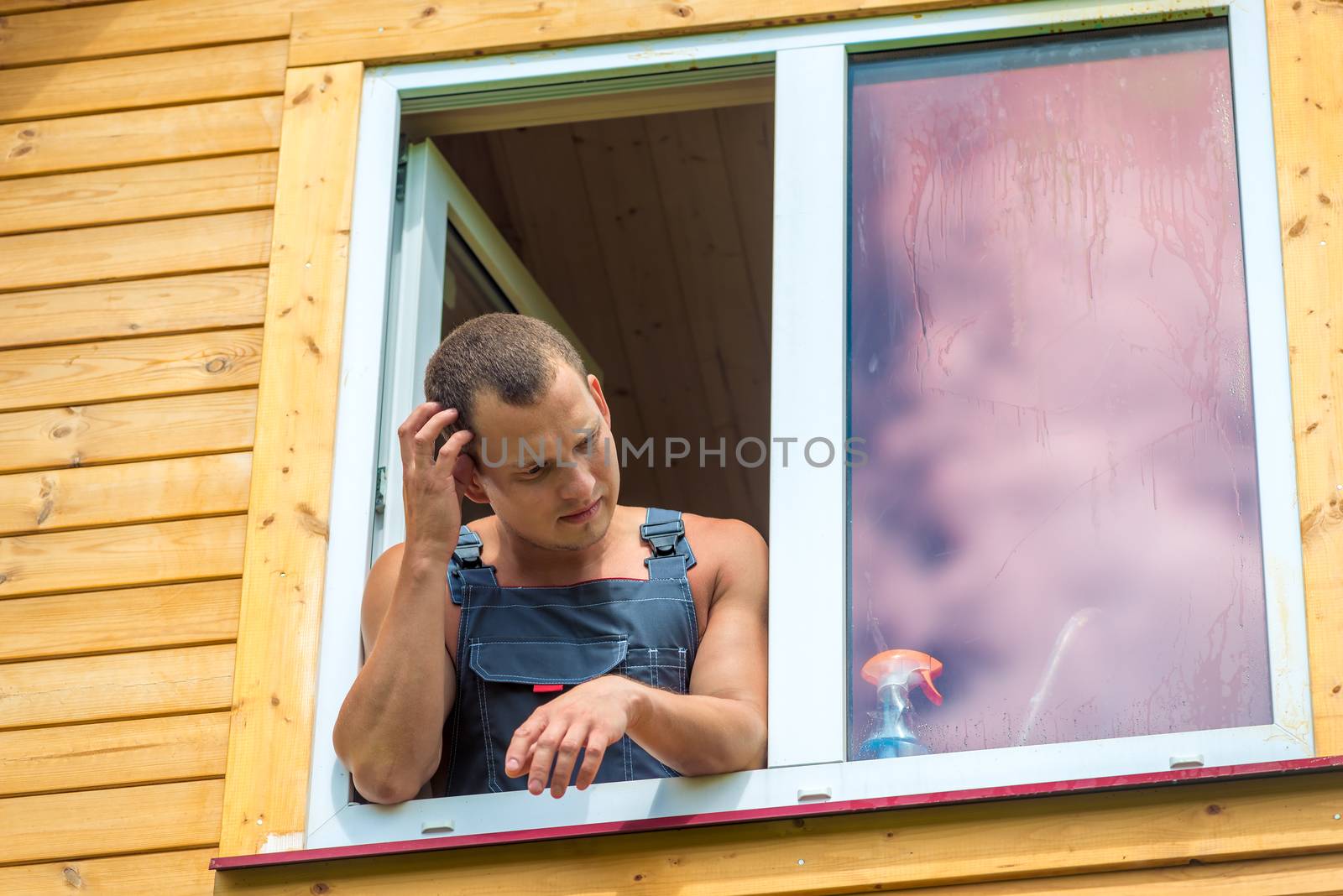 Pensive man in overalls reflects on washing the window in the ho by kosmsos111