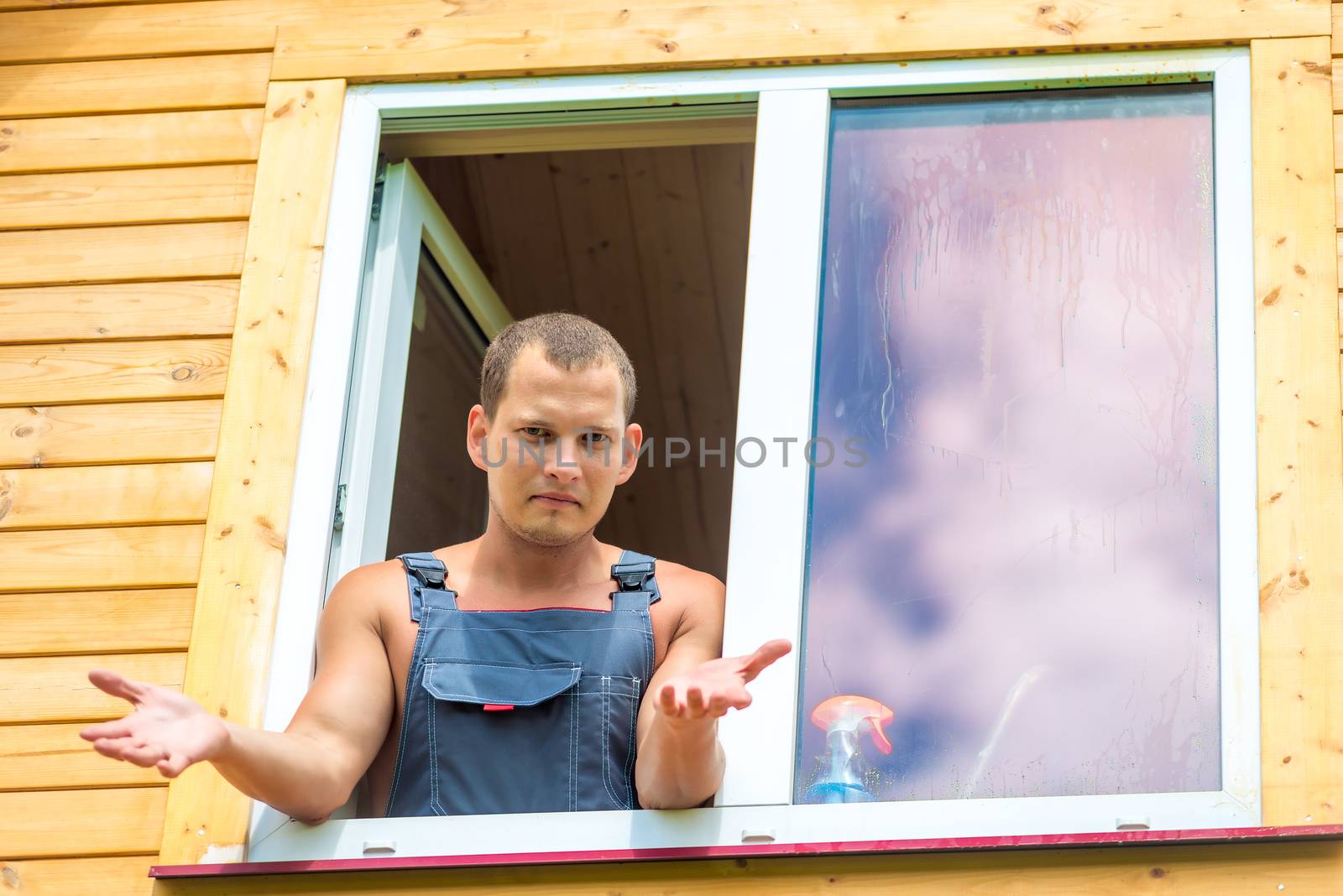 Discouraged man in overalls reflects on washing the window in the house