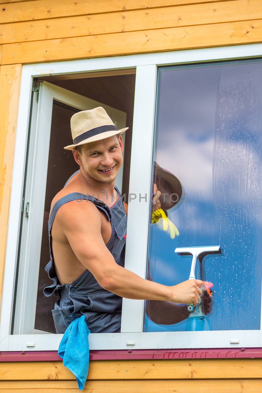 Sexy man in overalls washes a window in a wooden house