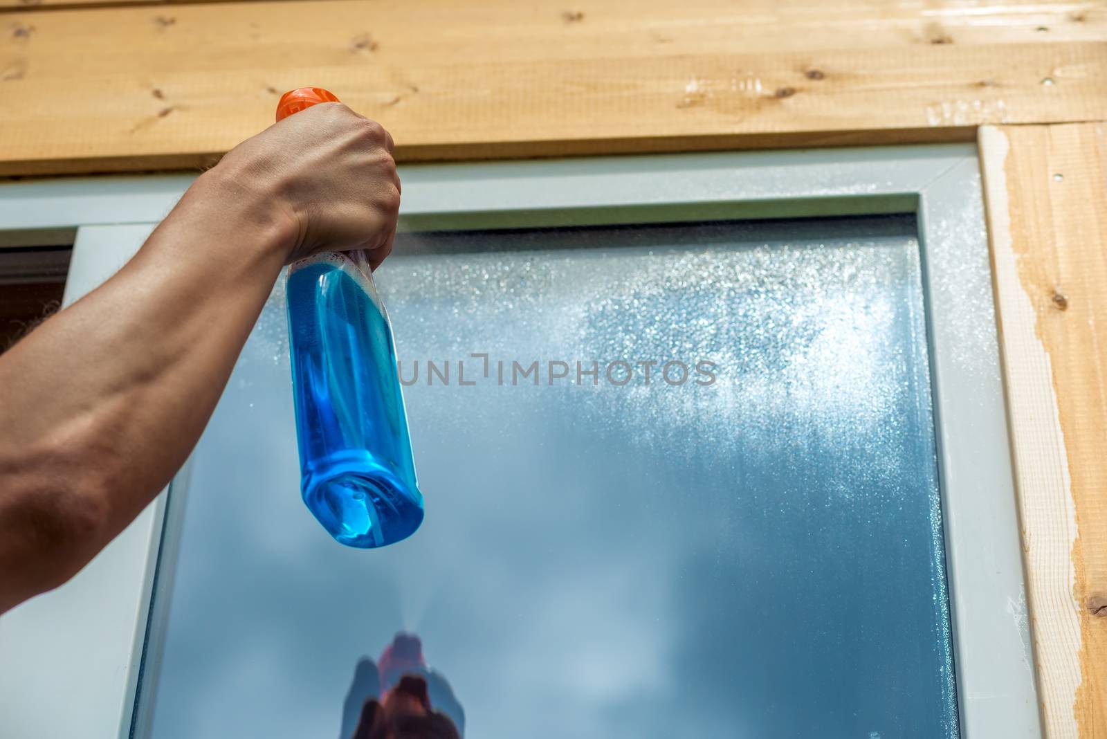 Washing window, closeup of spray cleaner in male hand on window background.