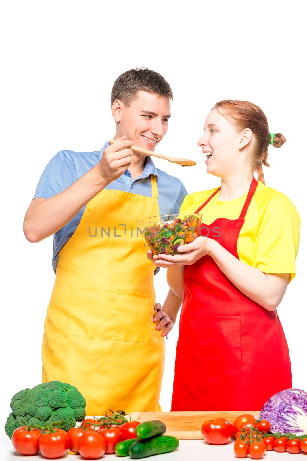 a man with a wooden spoon and a girl with a bowl of salad try the food cooked together on a white background