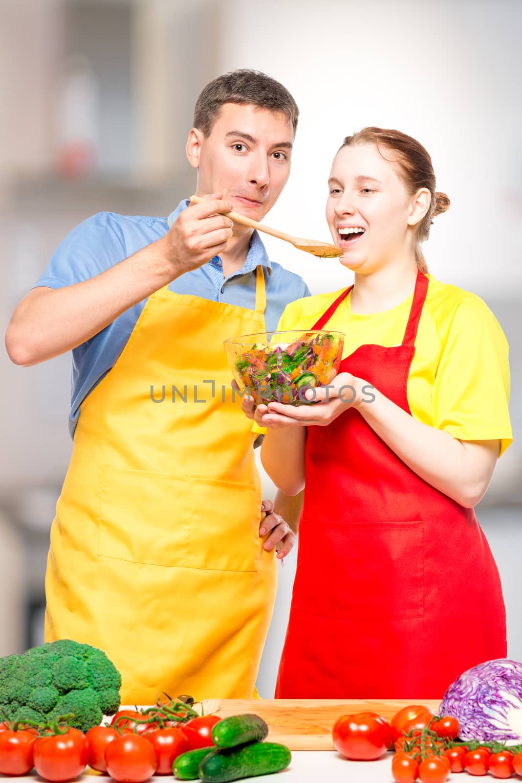 a man with a wooden spoon feeds a girl with a useful vegetable salad in the kitchen