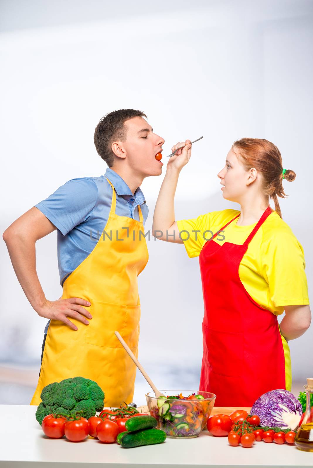 a woman with a wooden spoon feeds a man a healthy vegetable salad in the kitchen
