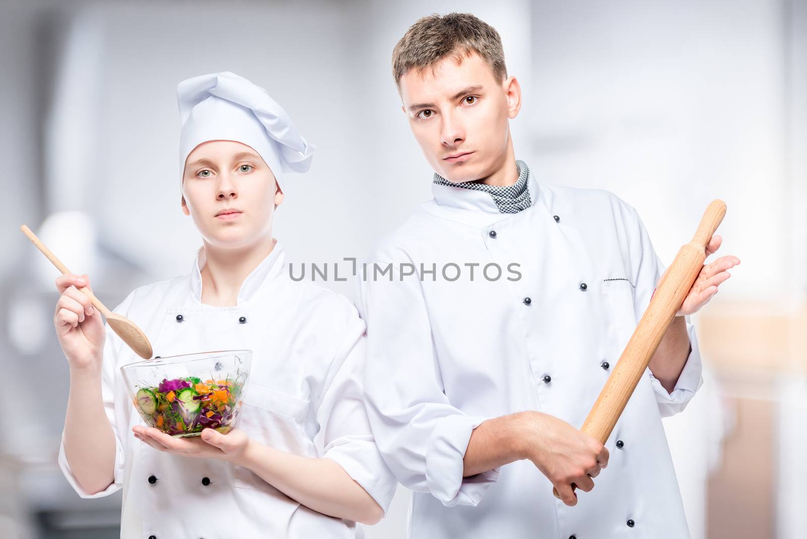 professional couple cooks with salad and rolling pin on a background of commercial kitchens