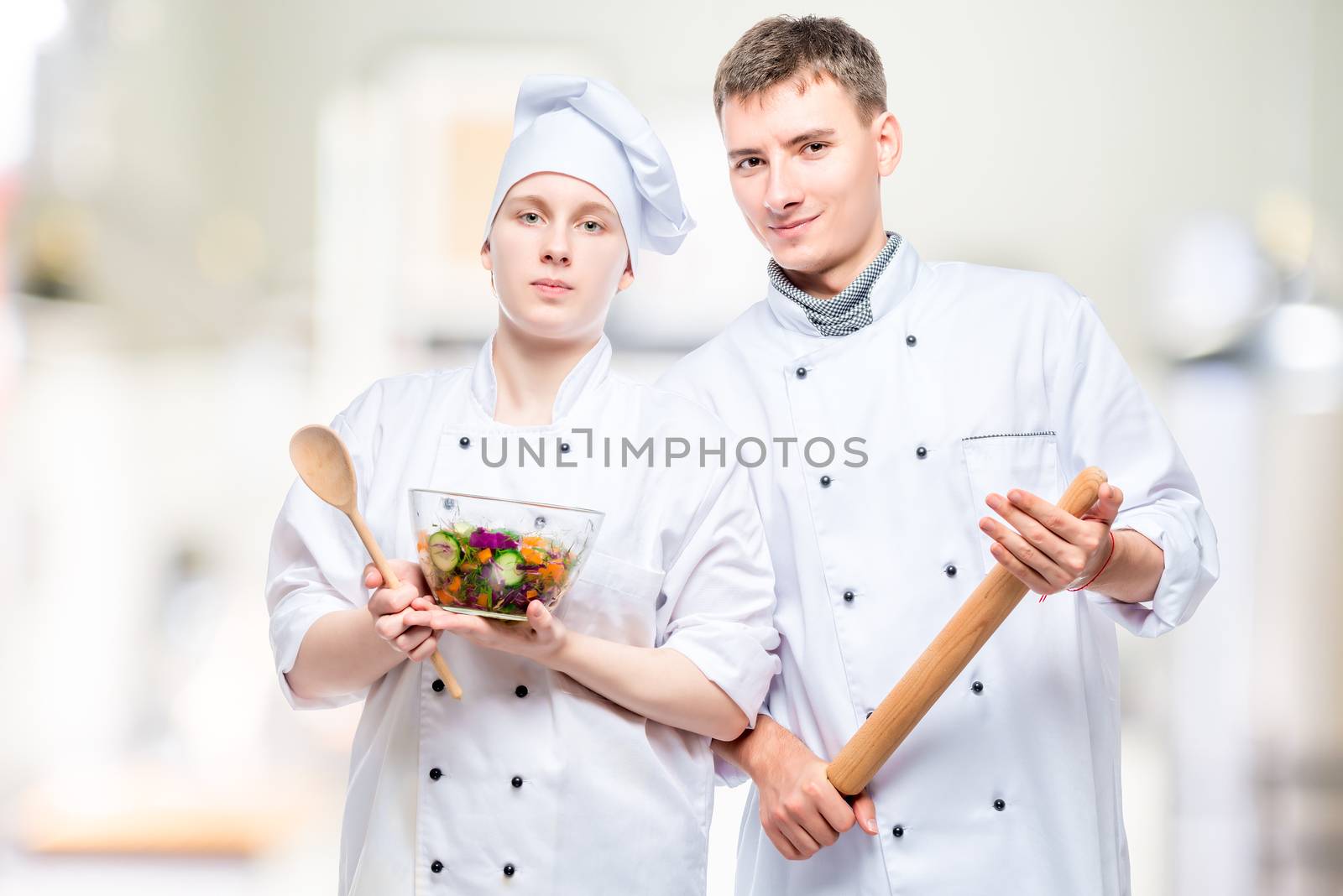 portrait of professional couple of cooks with salad and rolling pin on the background of commercial kitchen