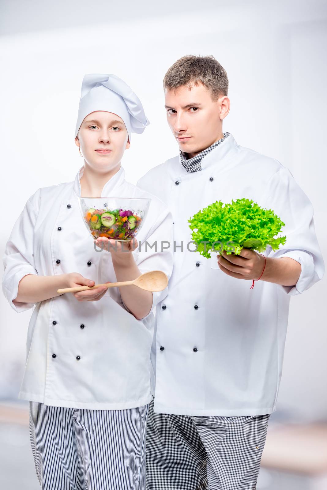 young cooks in suits with salad in hands on gray background by kosmsos111
