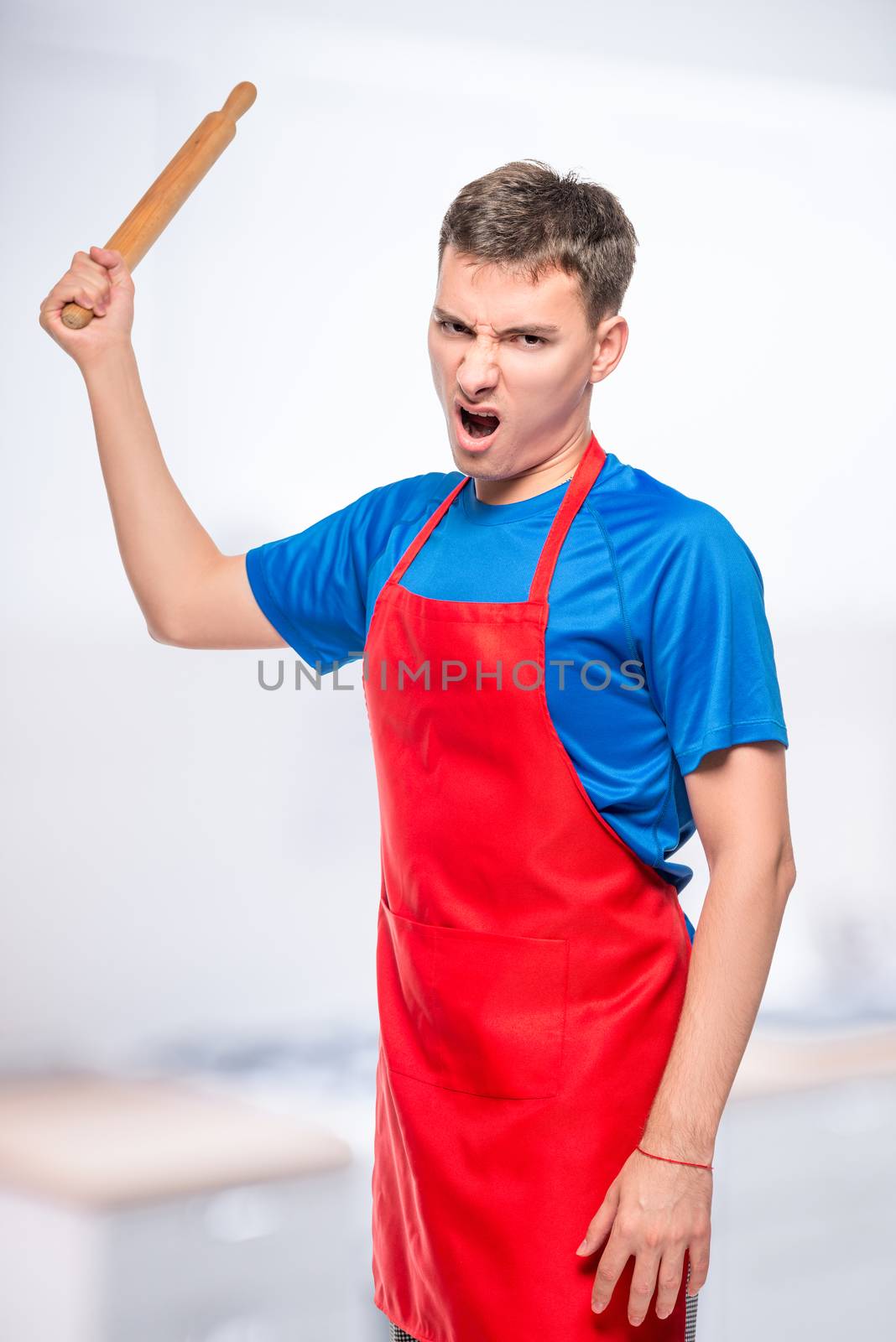 angry man in an apron with a rolling pin, a portrait on the background of the kitchen