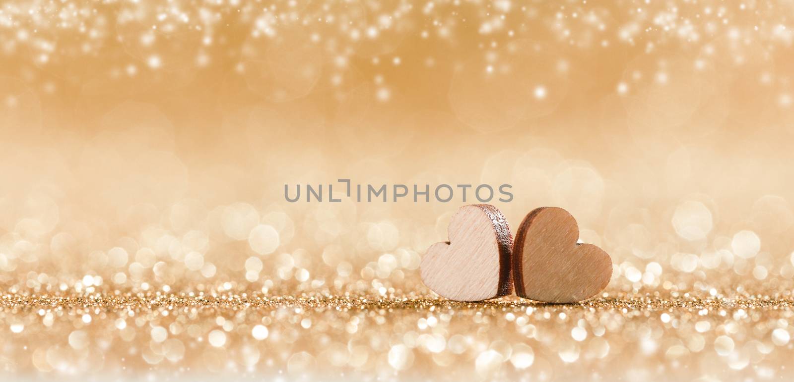 Two small handmade wooden hearts on golden bright lights bokeh background