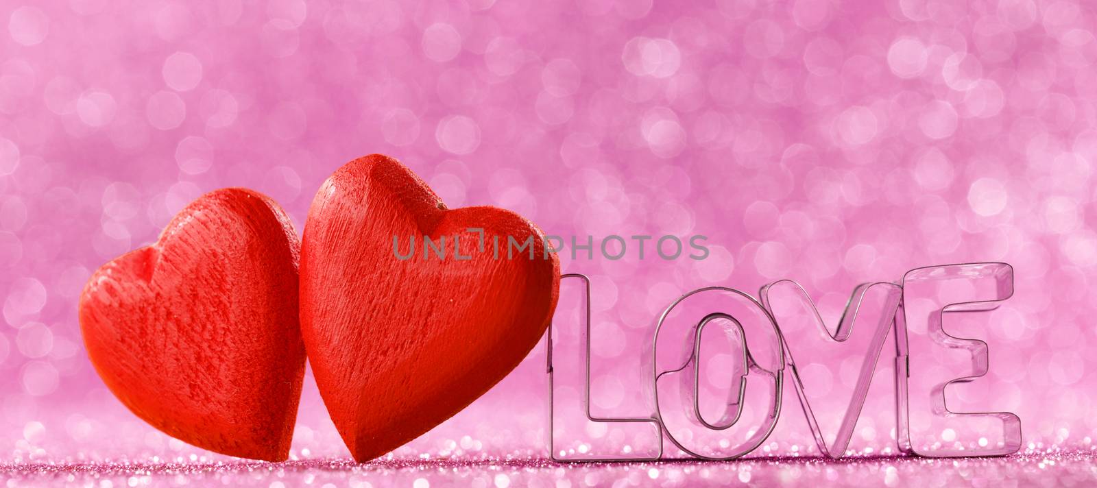 Two red handmade wooden hearts and word love on pink bright glitter lights bokeh background