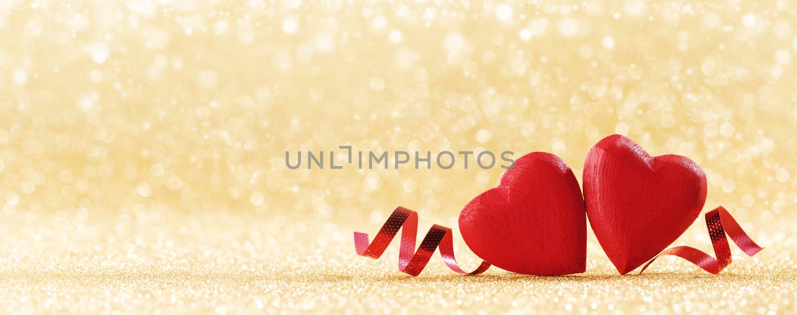 Two red handmade wooden hearts and ribbons on golden bright glitter lights bokeh background