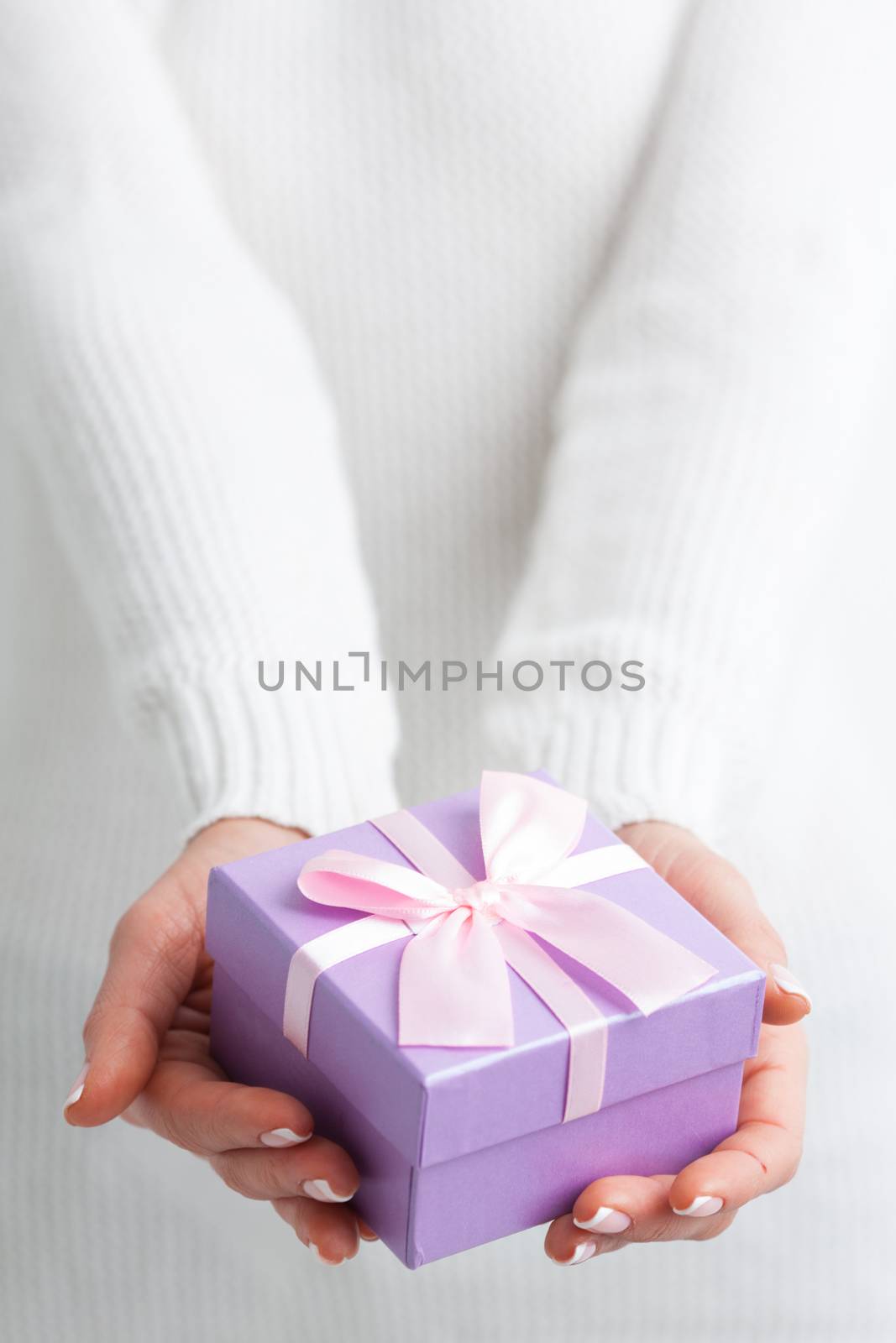 Female hands holding purple gift box with pink ribbon