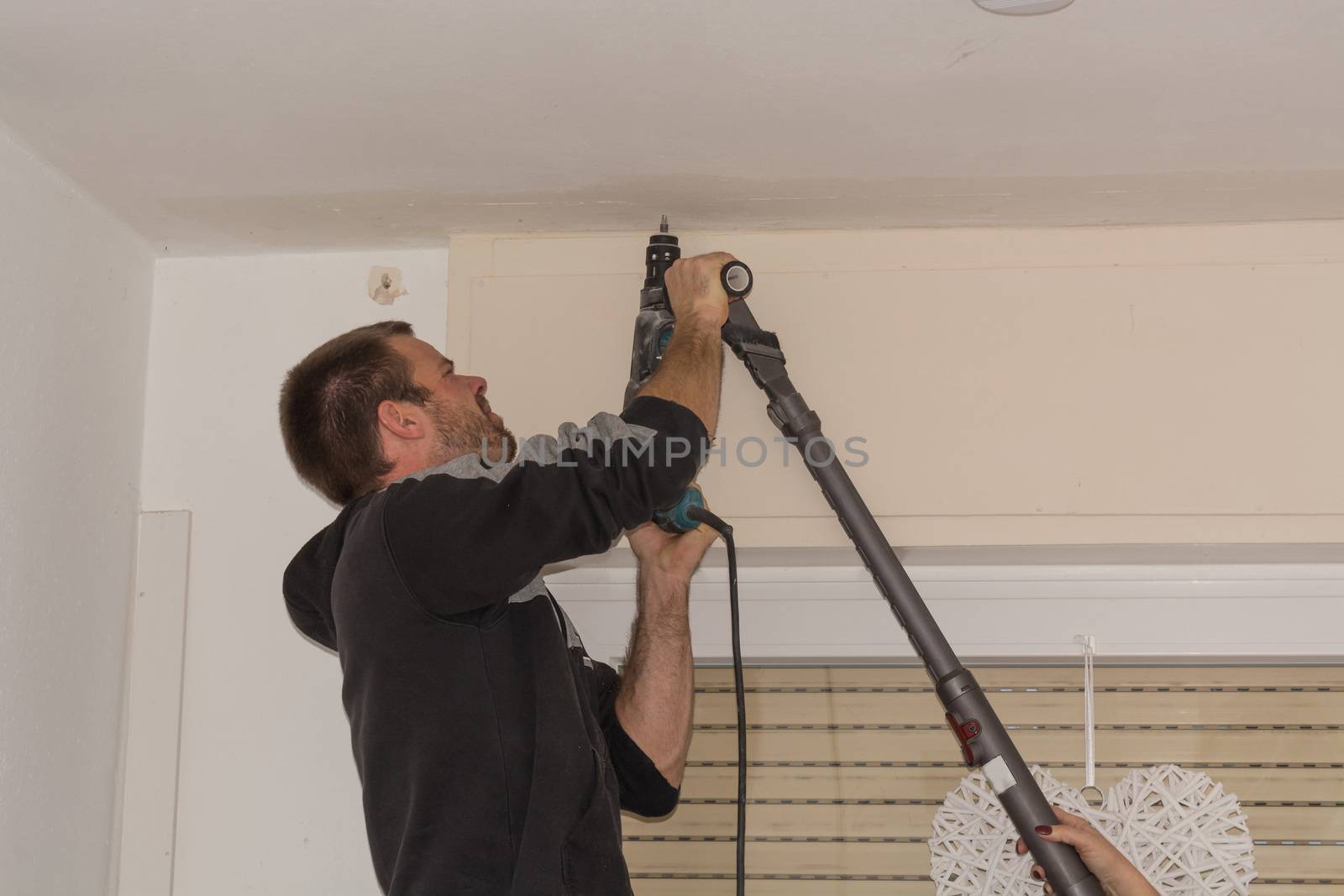 The man drills a hole in the ceiling before mounting a curtain rod