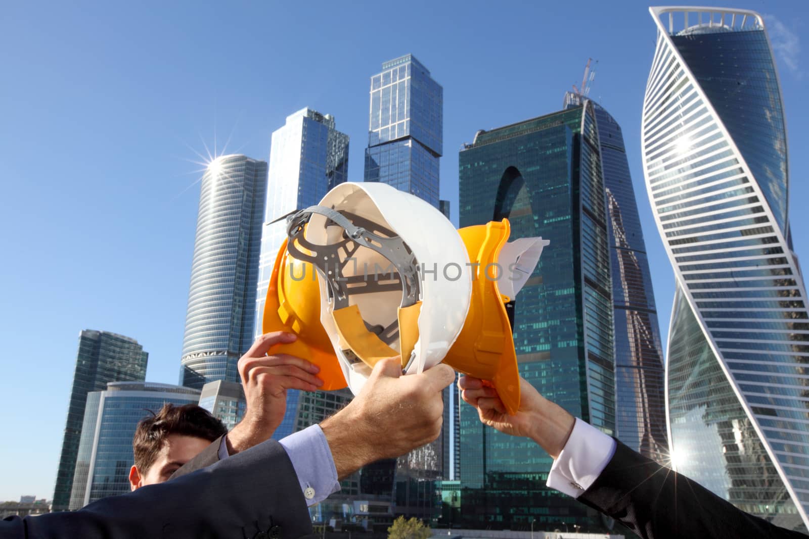 Group of business people clinking their helmets as a success on skyscrapers background, construction finished concept