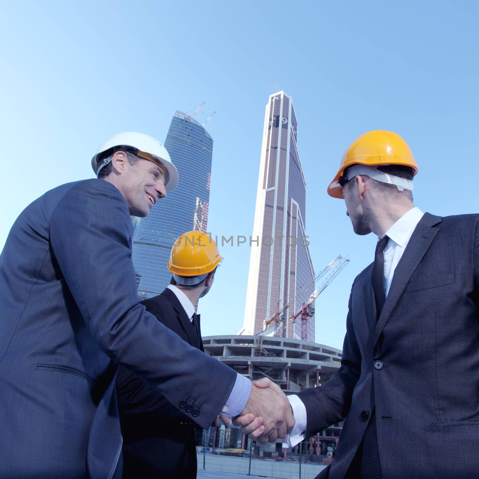 Architects wearing helmets shaking hands at skyscrapers background