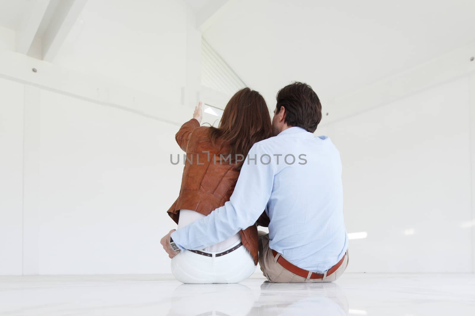 Young couple sitting on the floor of new empty house and pointing up into the air