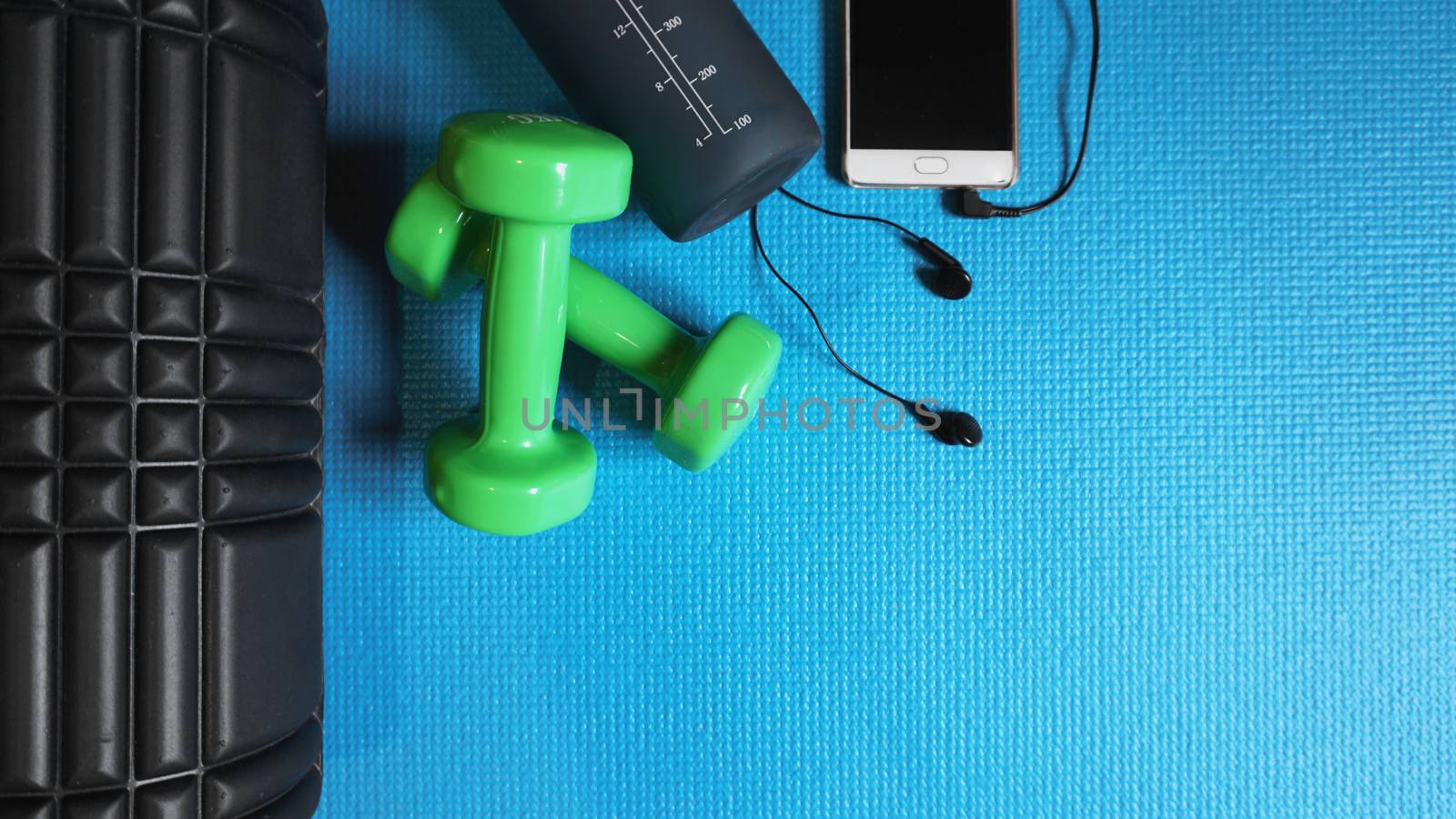 Foam Roller with green dumbbells and water bottle and telephone with headphones - Gym Fitness Equipment Blue background self Myofascial Release - MFR.