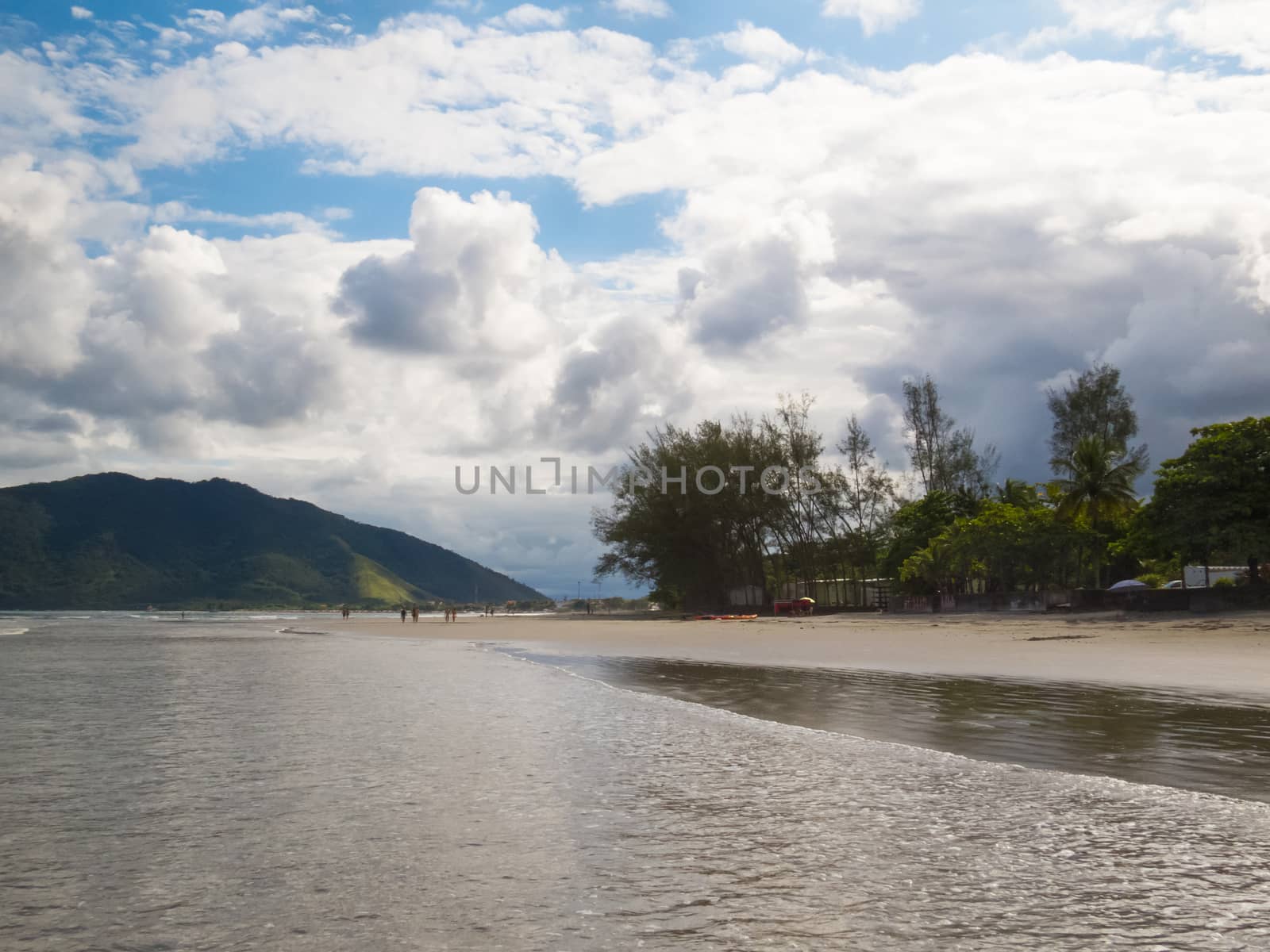 Sunny beach with green hills and woods in the background, and clouds in the sky.