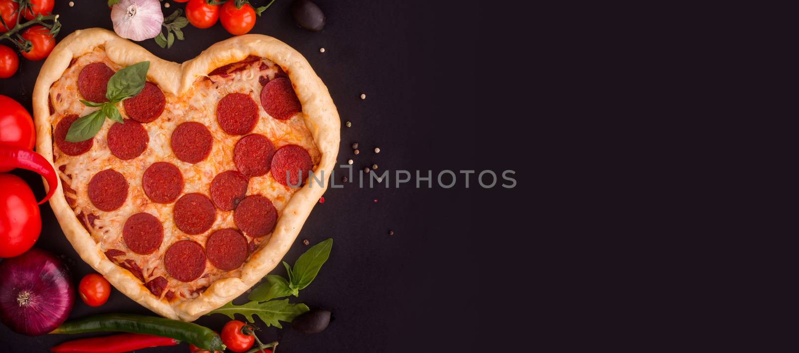 Pizza heart shaped with pepperoni with ingredients on black background. Concept of romantic love for Valentines Day . Love food