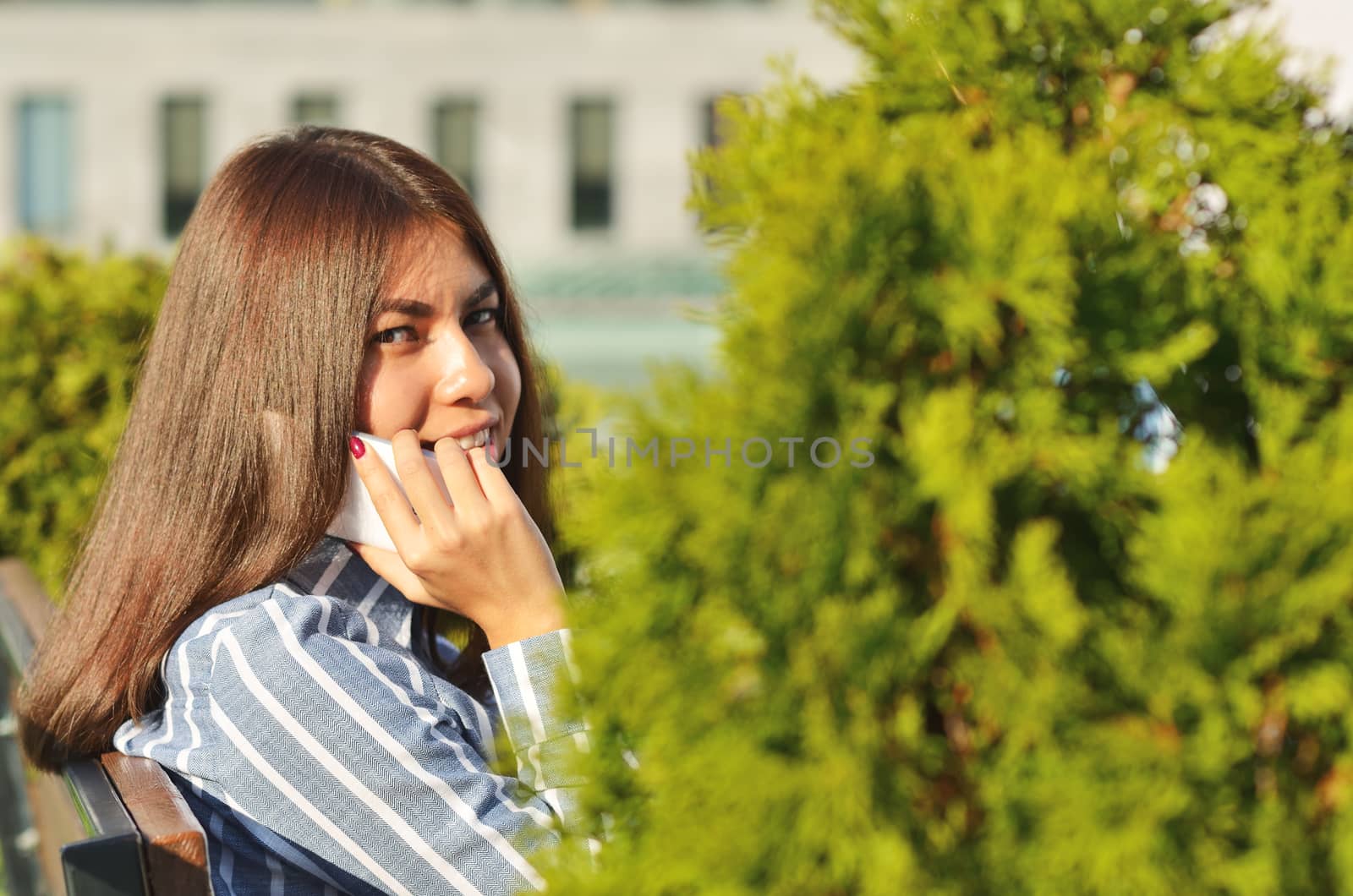 Beautiful portrait of a young girl who talks on the phone in the city Park near the beautiful green spaces