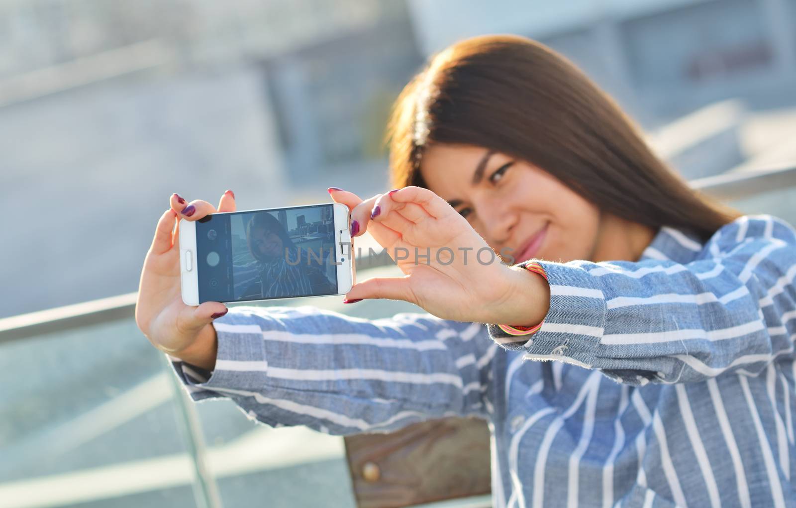 A young girl photographs herself with a phone, walking around the city