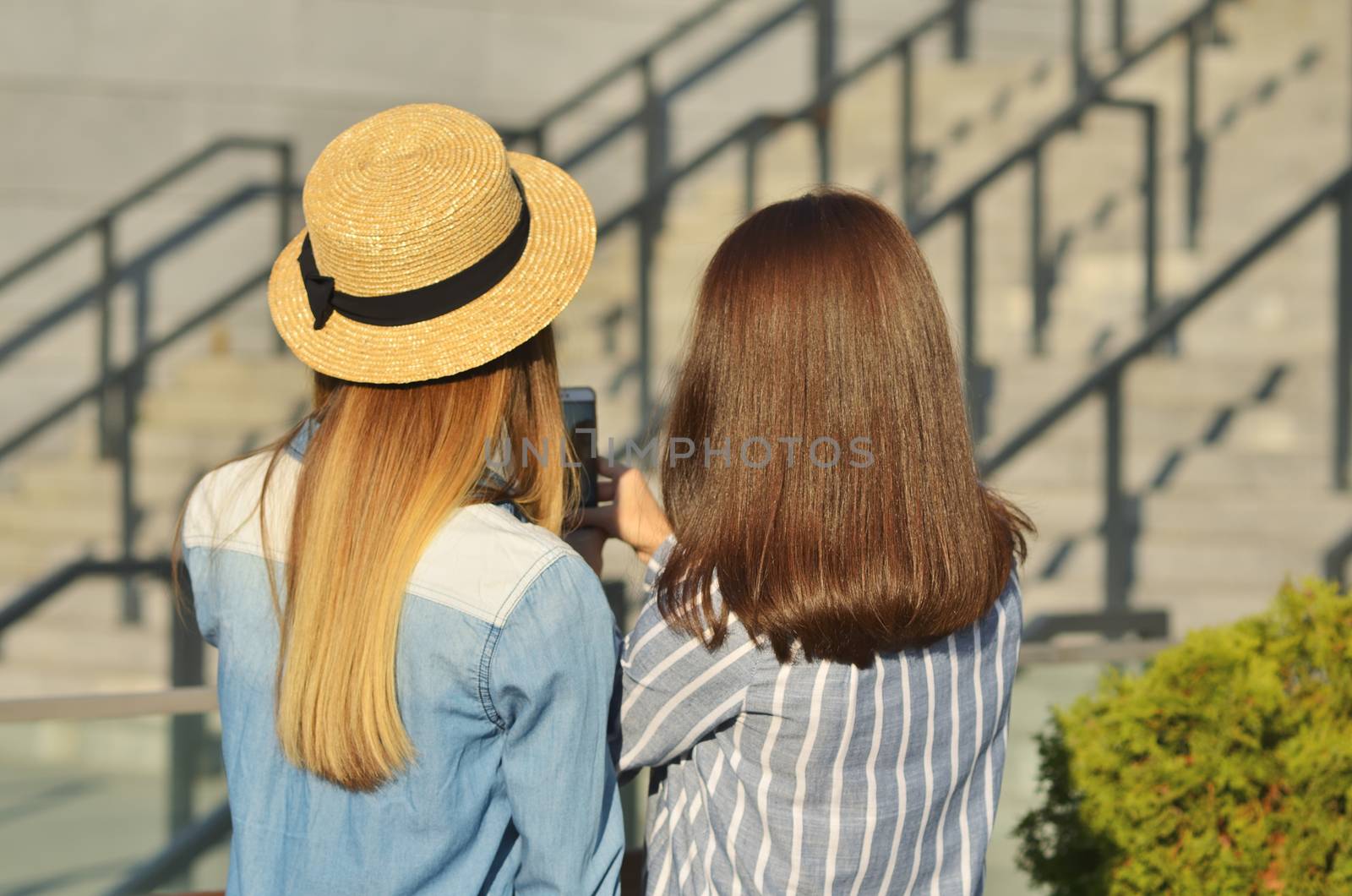 Two young girl friends take a selfie walking on the street in the city Park