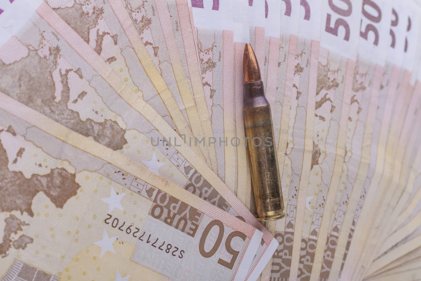 Single rifle bullet closeup with a pile of euro banknotes in the background