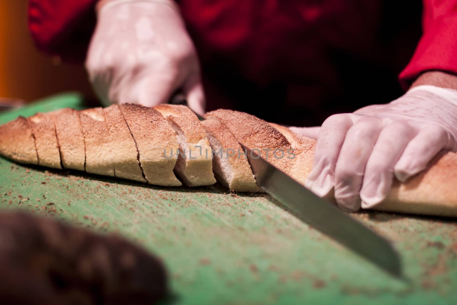 Slicing fresh baked bread with long knife moving hands 