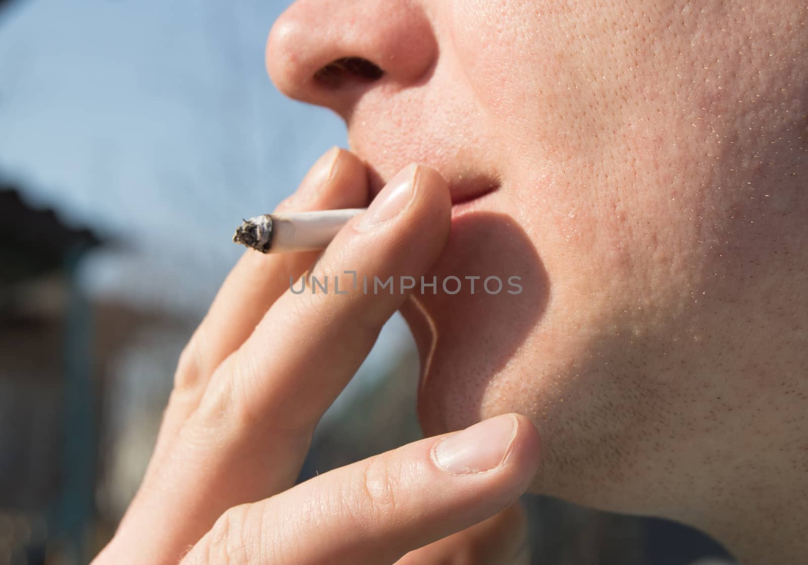 Young handsome man holding a cigarette in his mouth. Stands against the blue sky by claire_lucia