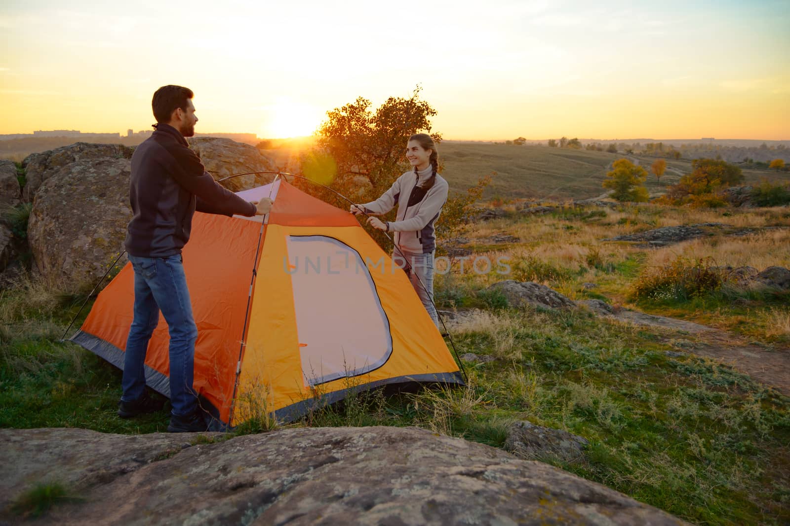 Young Couple Assembling the Tent at Sunset in the Mountains. Adventure and Family Travel. by maxpro