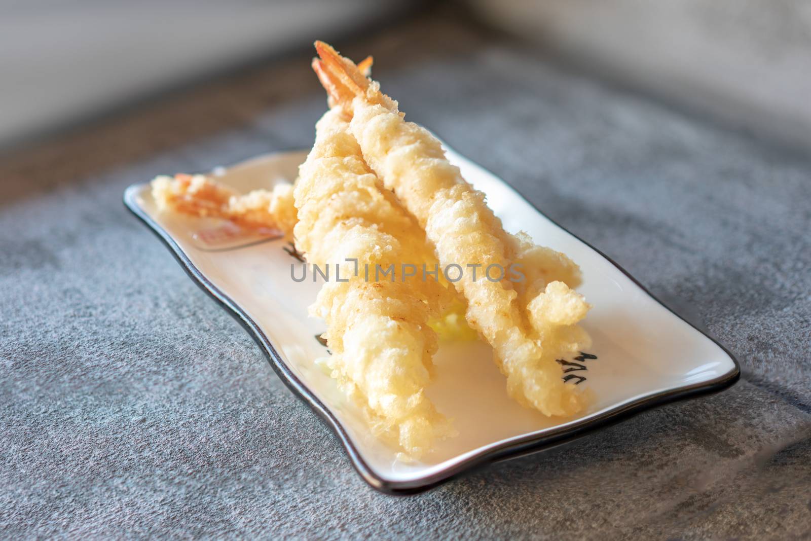 Tempura prawn served  on rectangular white plate on dark gray stone background