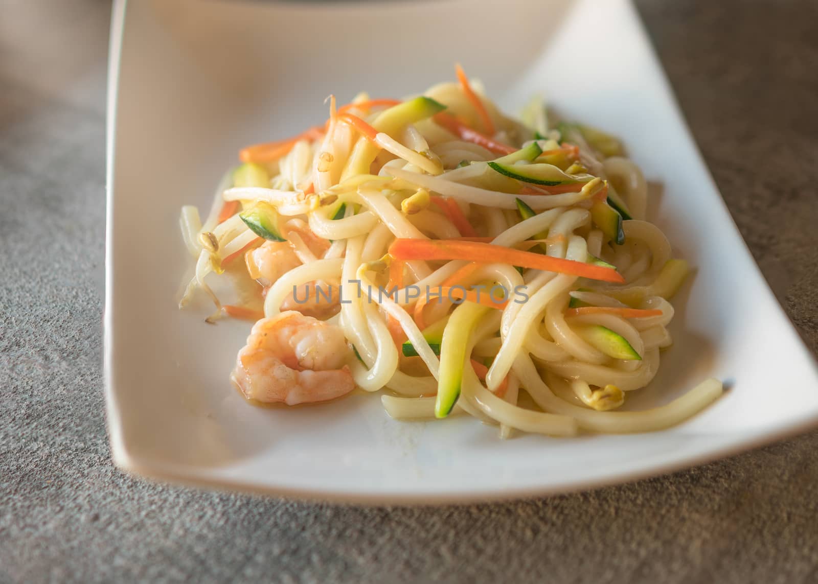 Yaki udon served  on rectangular white plate on dark gray stone background