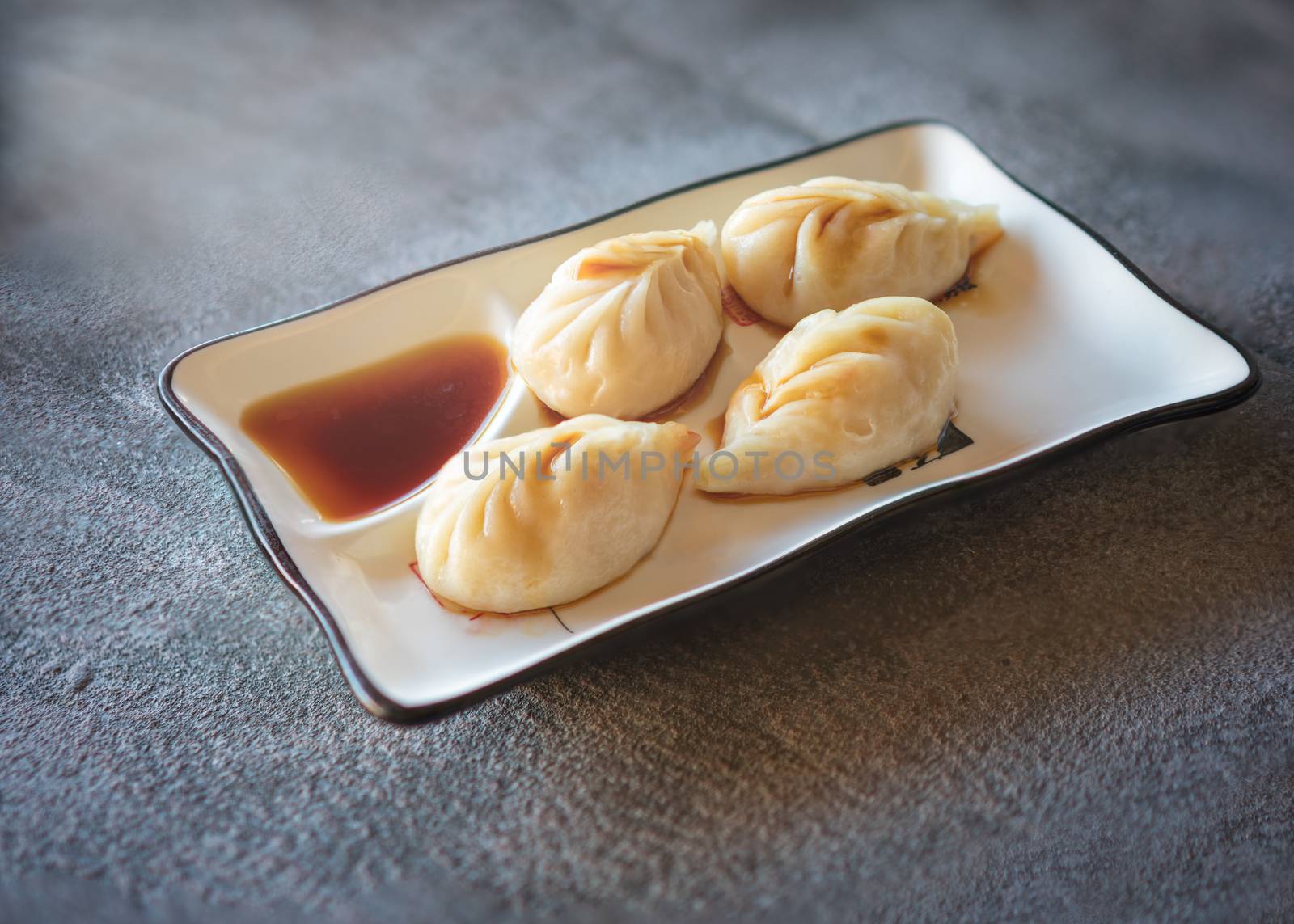 chinese steamed rolls served  on rectangular white plate on dark gray stone background