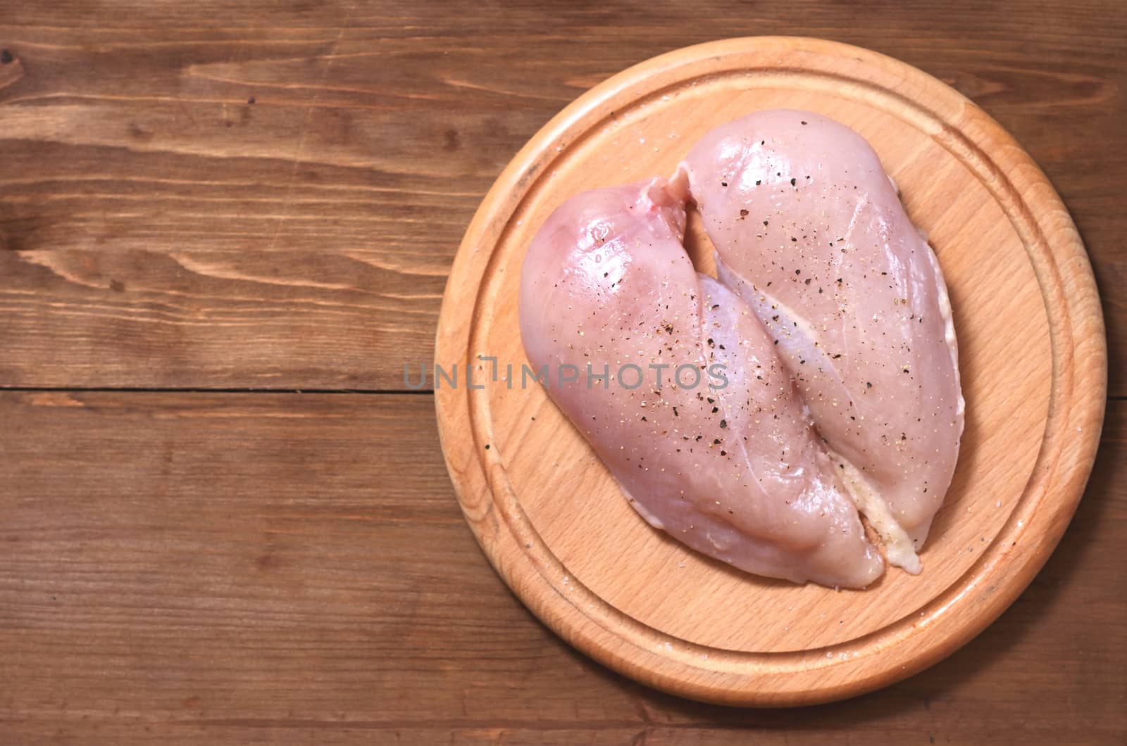 Two raw chicken fillets lie to the right in the shape of a heart on a wooden Board against a tree background. Meat is located in the center
