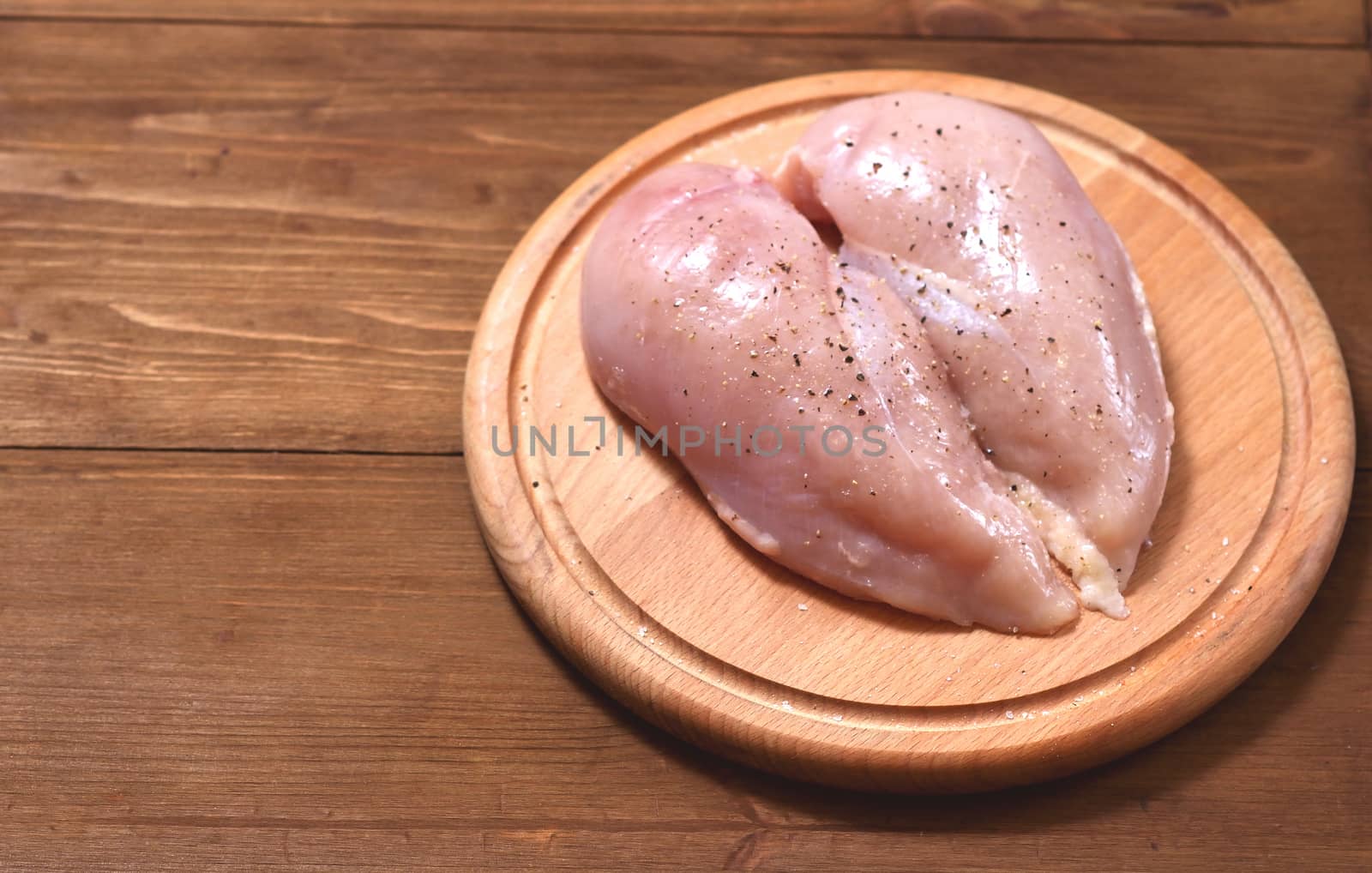 Two raw chicken fillets lie to the right in the shape of a heart on a wooden Board against a tree background. Meat is located in the center
