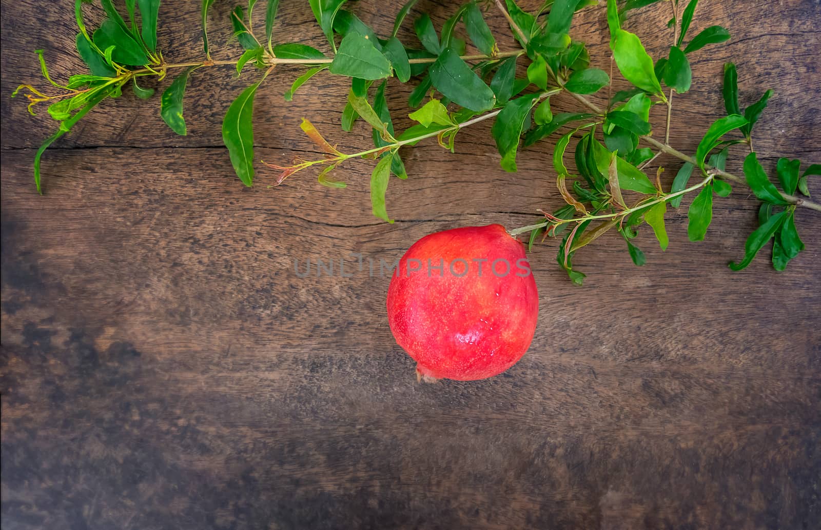 still life of red pomegranate with green leaves on wooden background with copy space