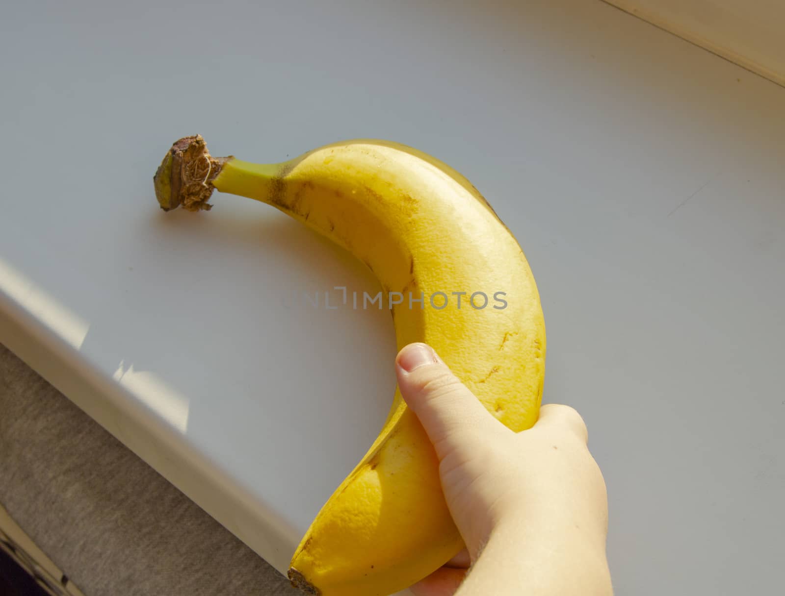 Healthy food for kids. Children's hand holding a banana, close-up, sunlight. by claire_lucia