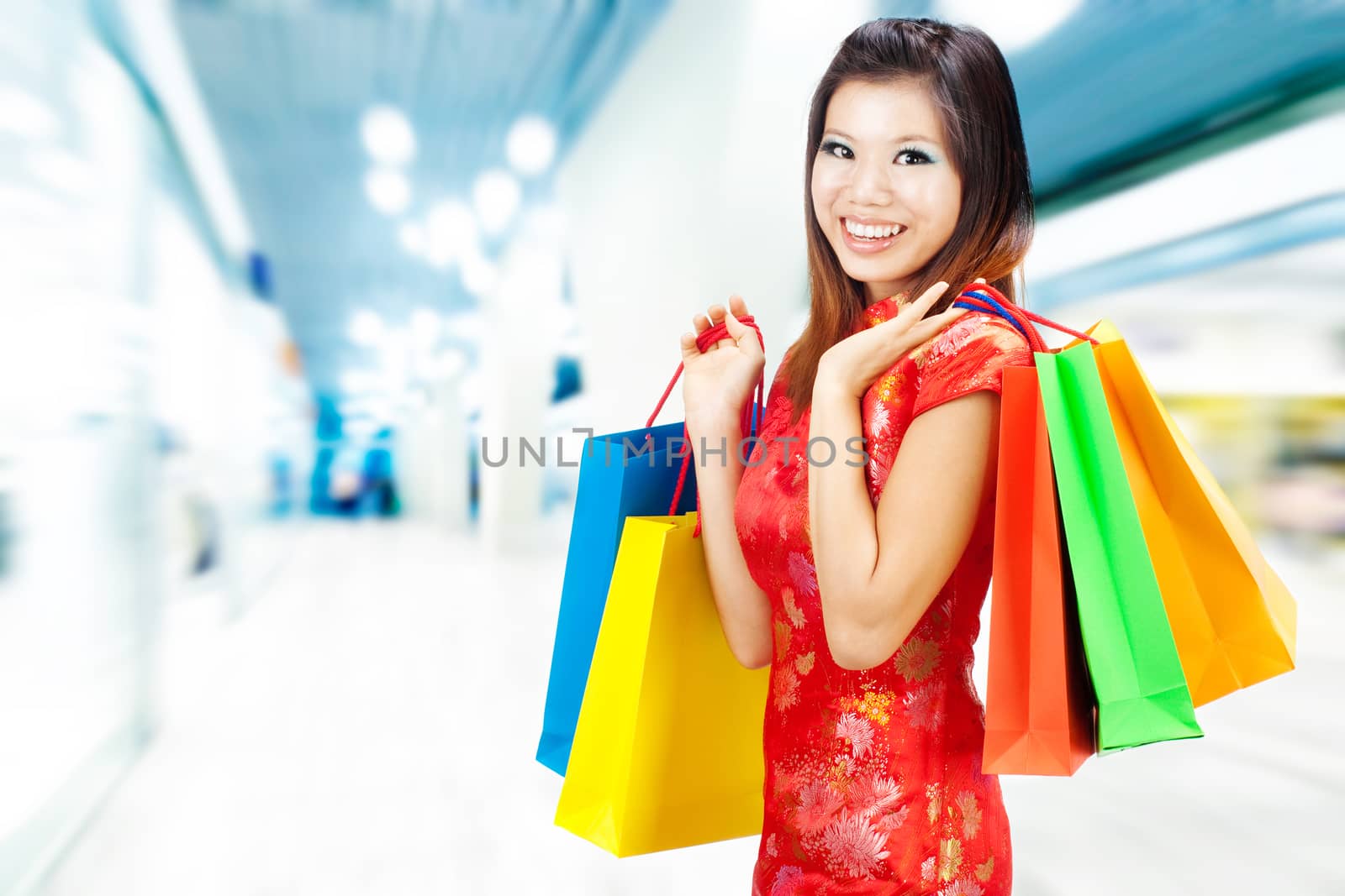 Oriental woman in red Traditional Chinese Cheongsam with shopping bag, standing inside mall.