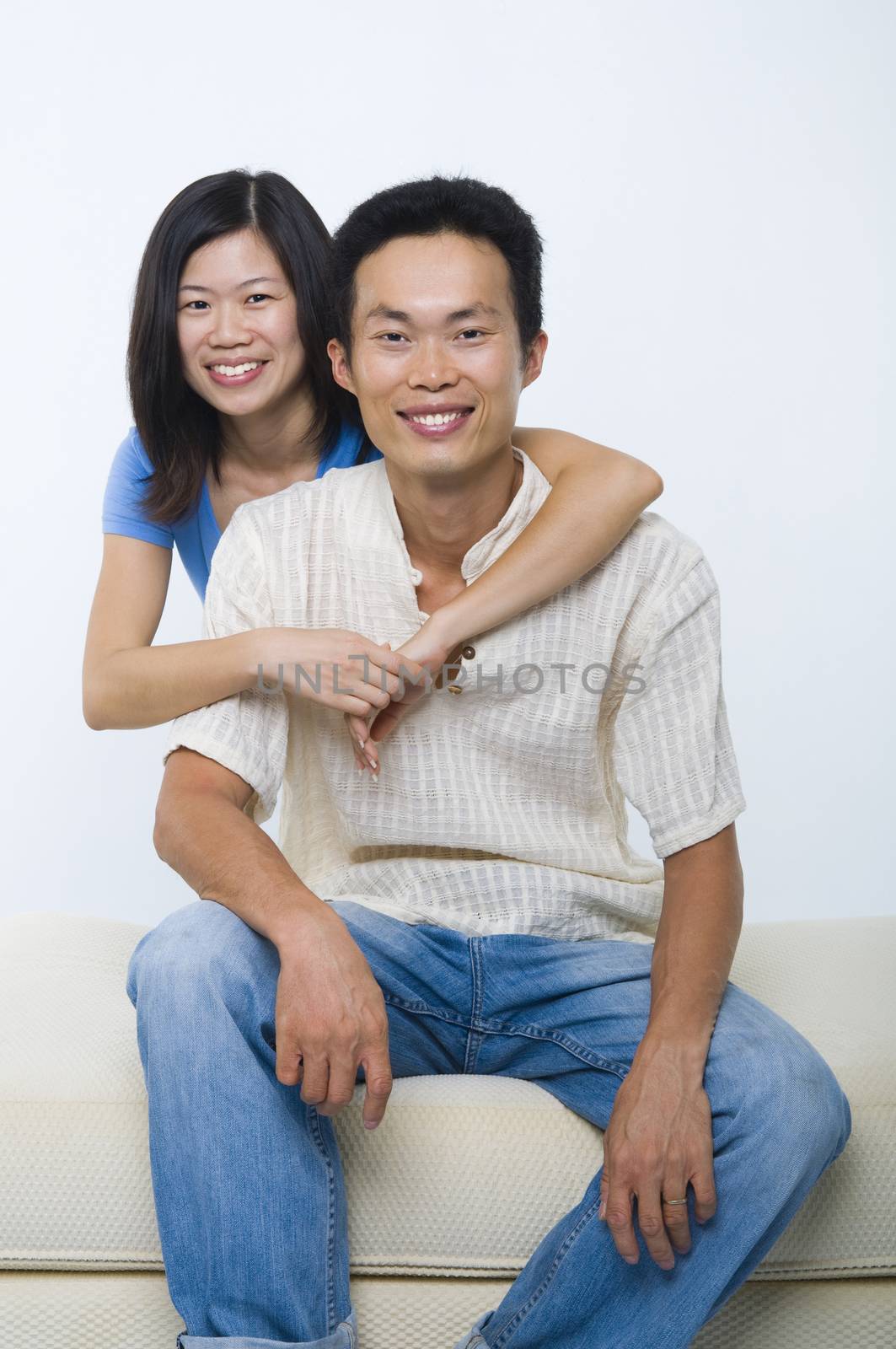 Young Asian couple sitting on sofa with smiling face, on white background.