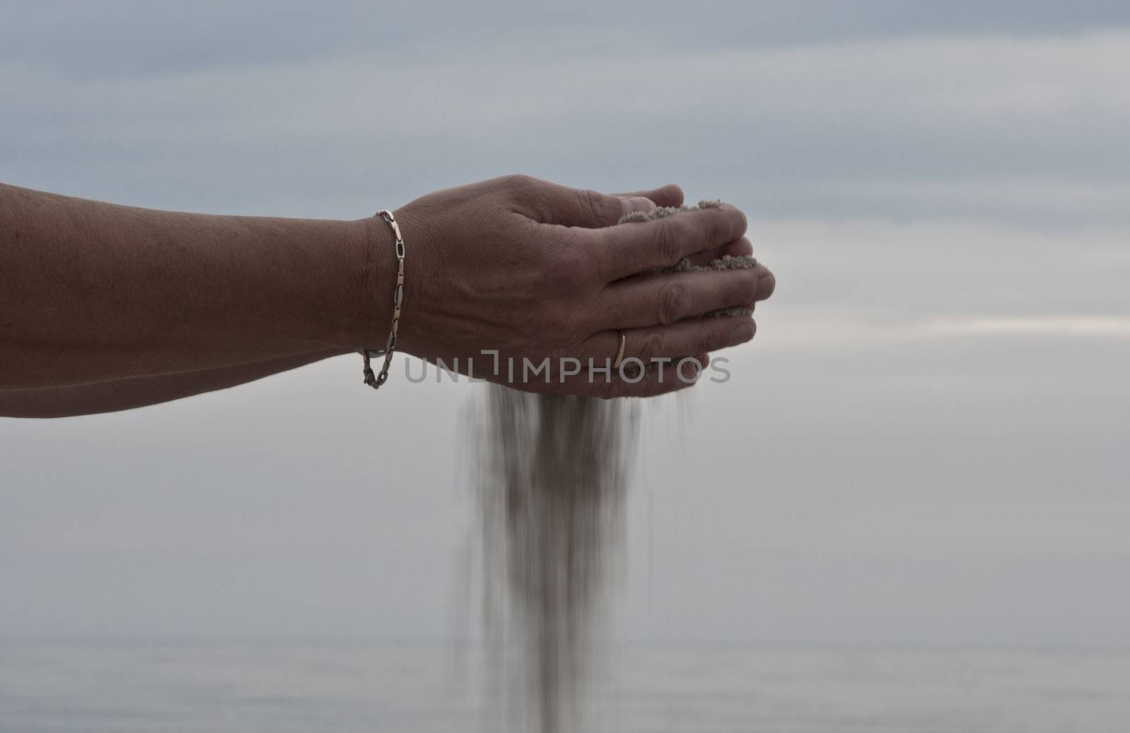 sand falls from the hand of a woman as an image of time passes