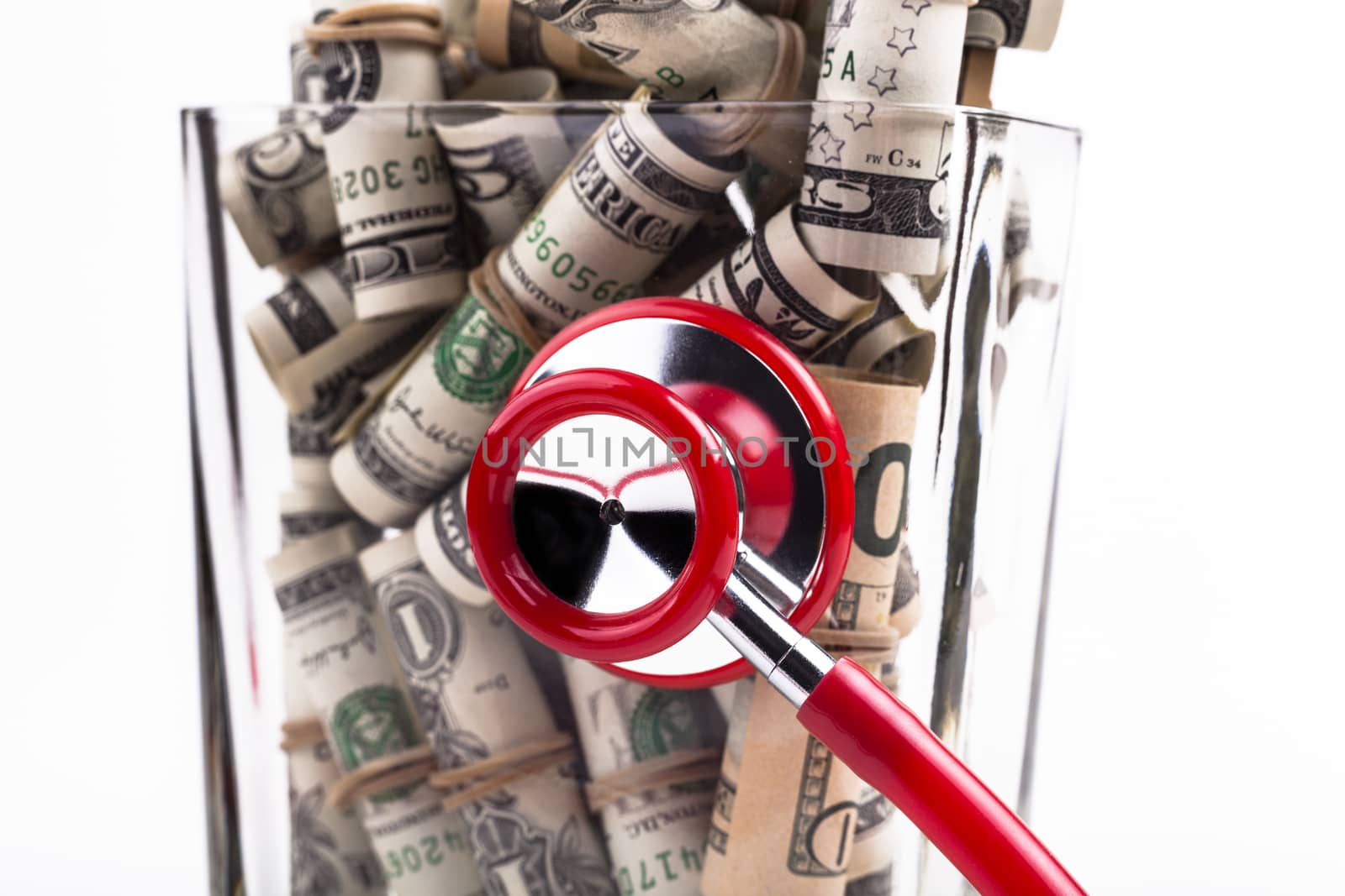 Health in a jar rolled dollars in ajar with a red stesthoscope close-up isolated on white background
