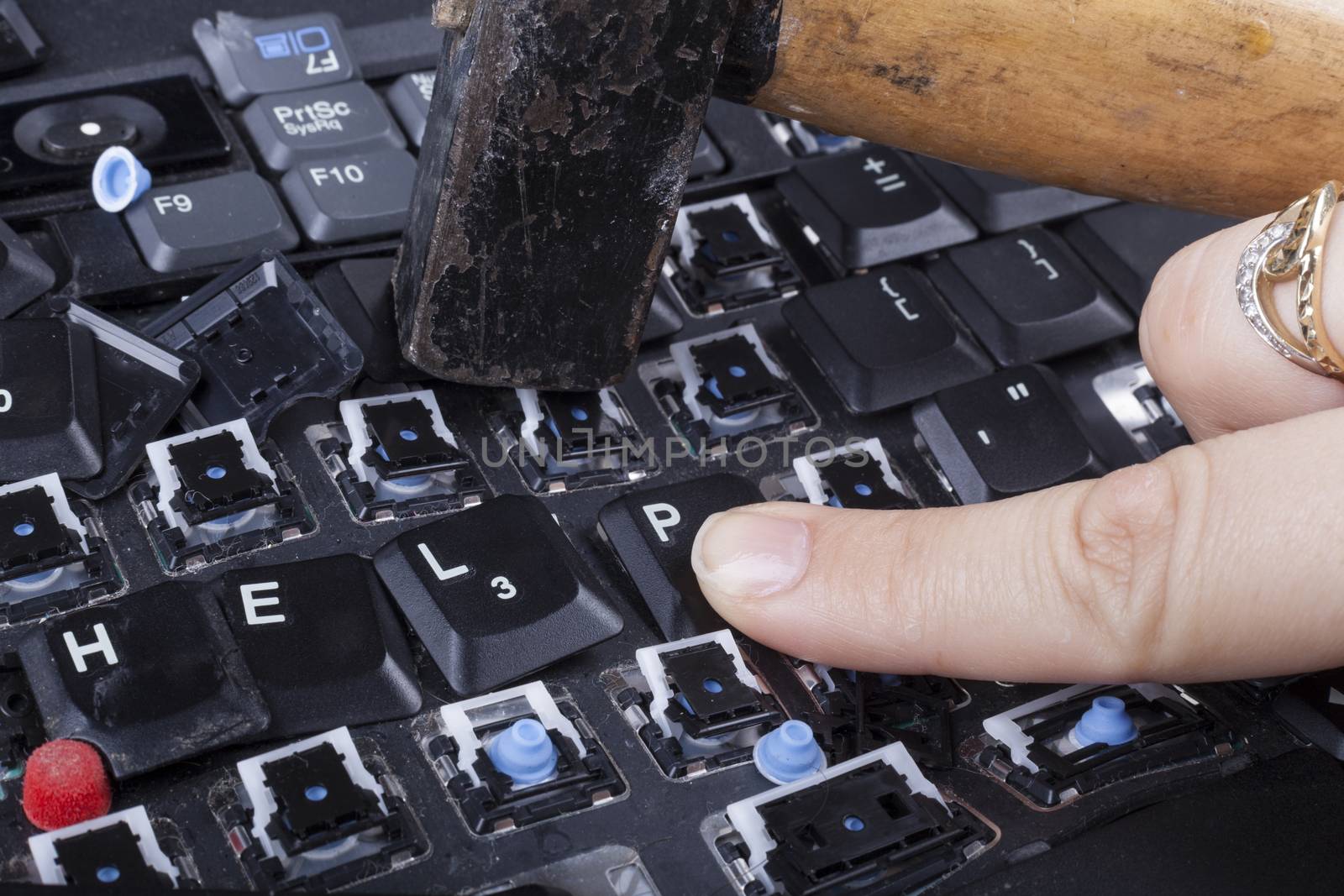 Woman finger on the help keys of broken keyboard with hammer in the background
