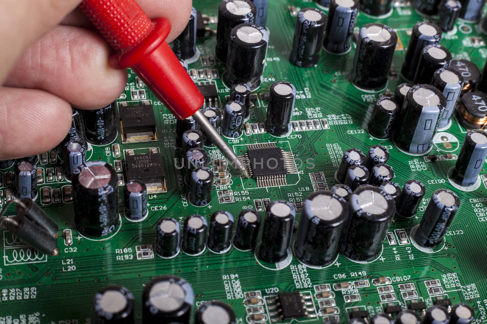 Electronics Repair service close-up with red probe and capacitors on electronic board