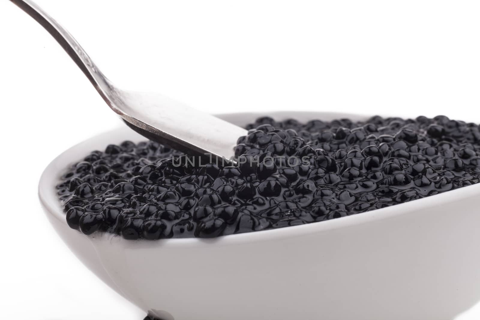 Black caviar beads in white bowl and silver spoon close-up isolated on white background