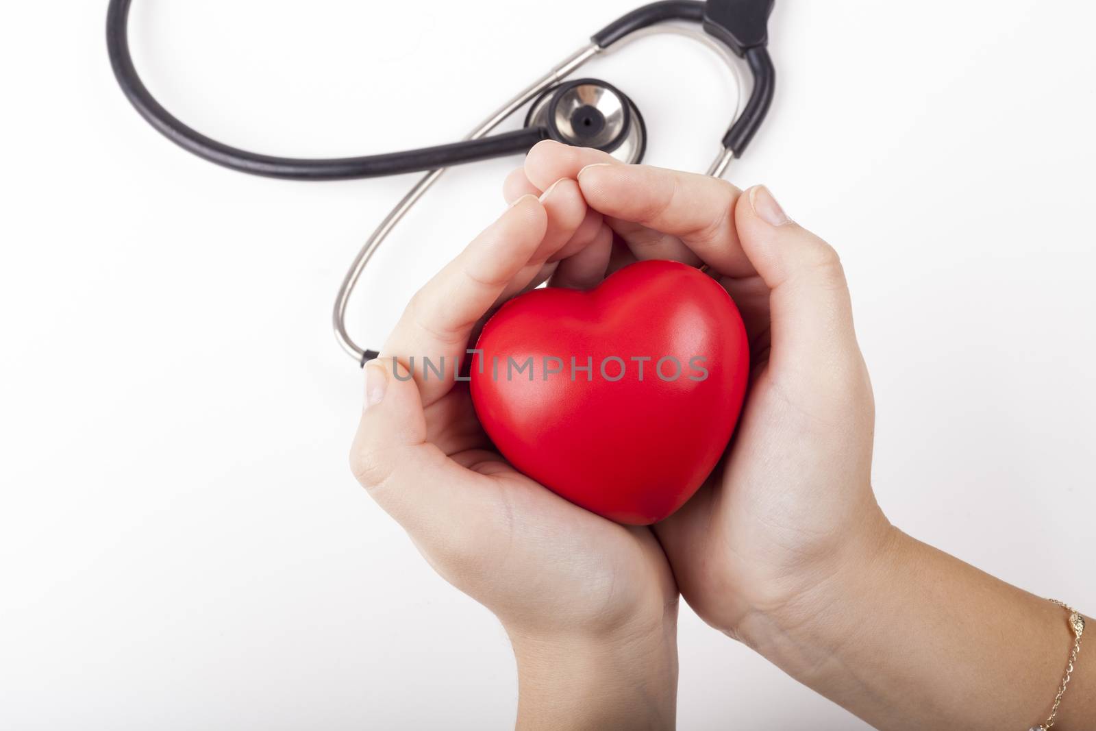 Holding red heart in two hands with black stethoscope in the background isolated on white