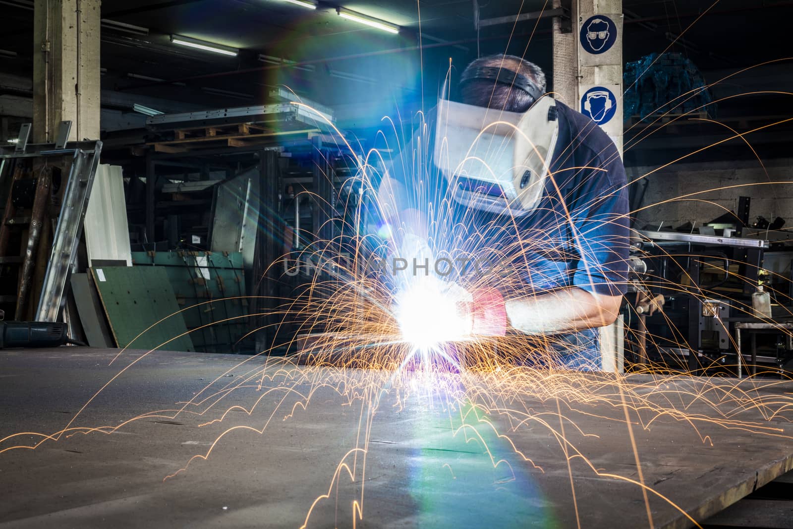 Worker welding in steel workshop with bright light and sparks