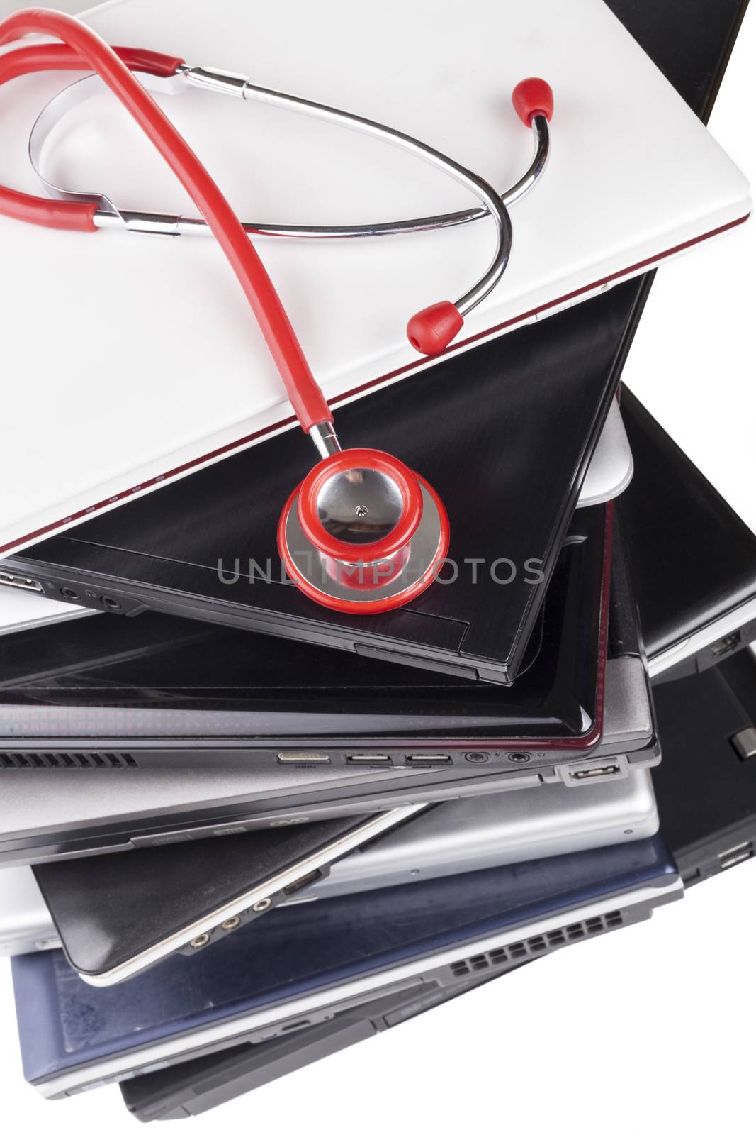 Red Stethoscope on pile of old laptops close-up upper view on white background