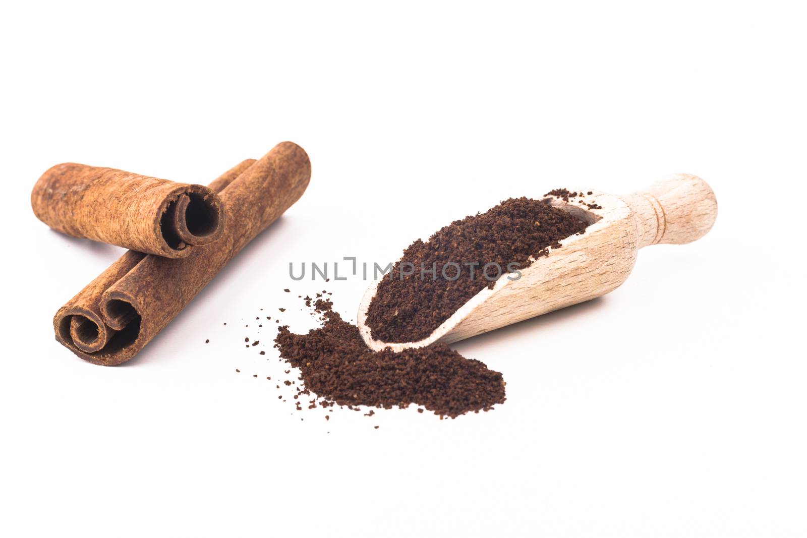 Grounded coffee in wooden spoon and cinnamon sticks isolated on white background
