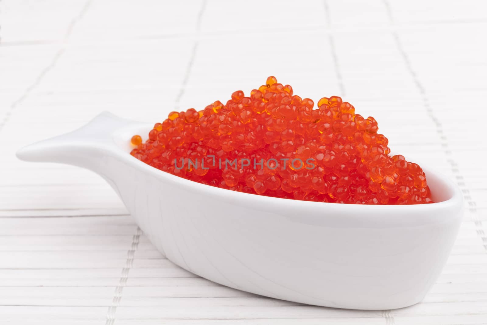 Red caviar in a fish shape bowl on white wooden background