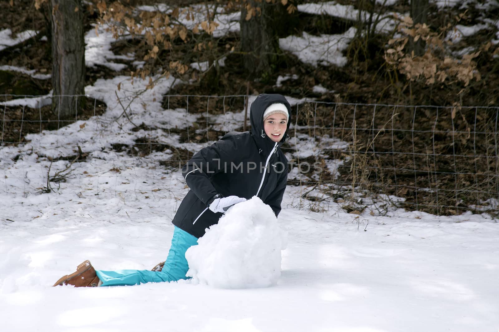 Teen girl in warm winter clothes making a snowman in the forest by Anelik